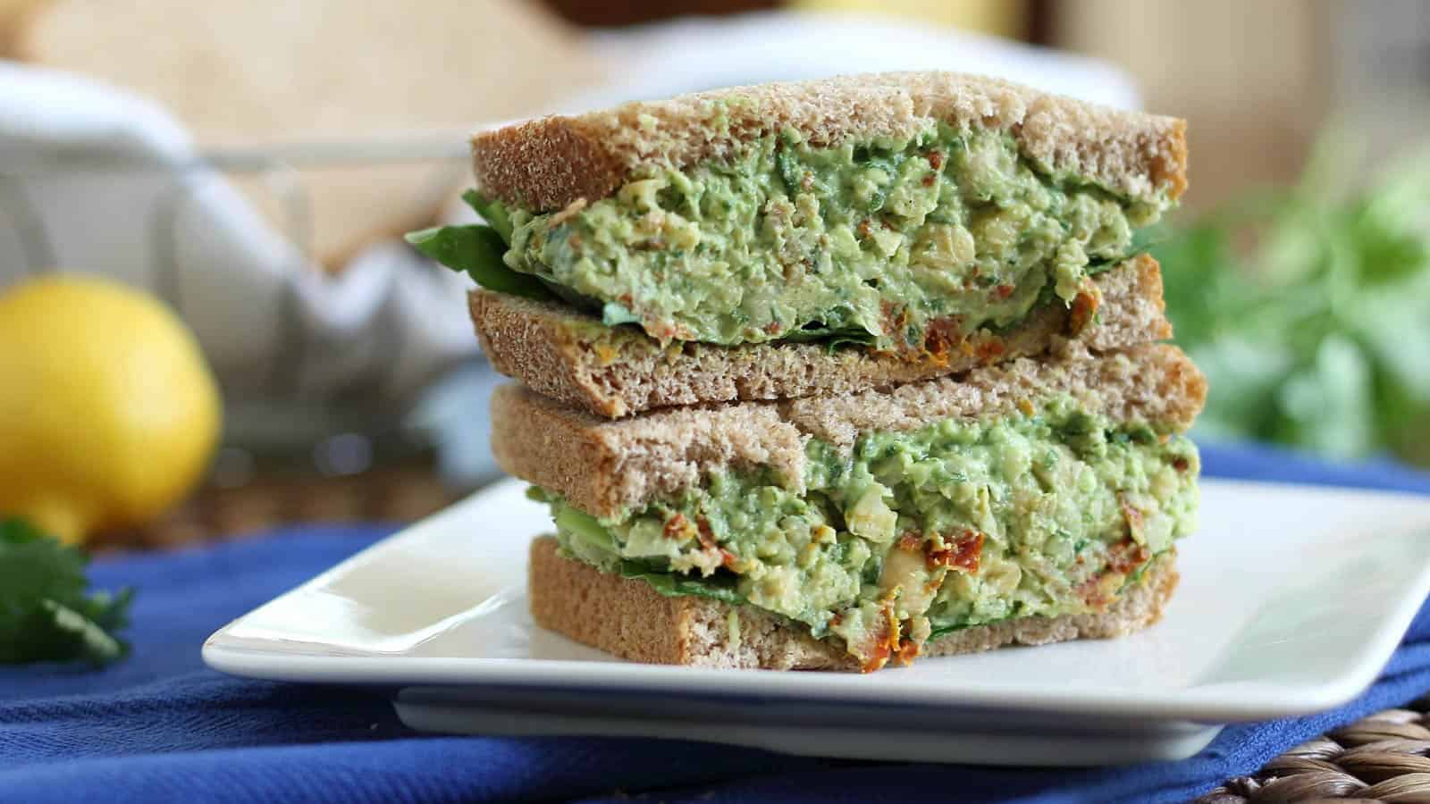 Chickpea pesto sandwich cut in half and stacked on a white plate.