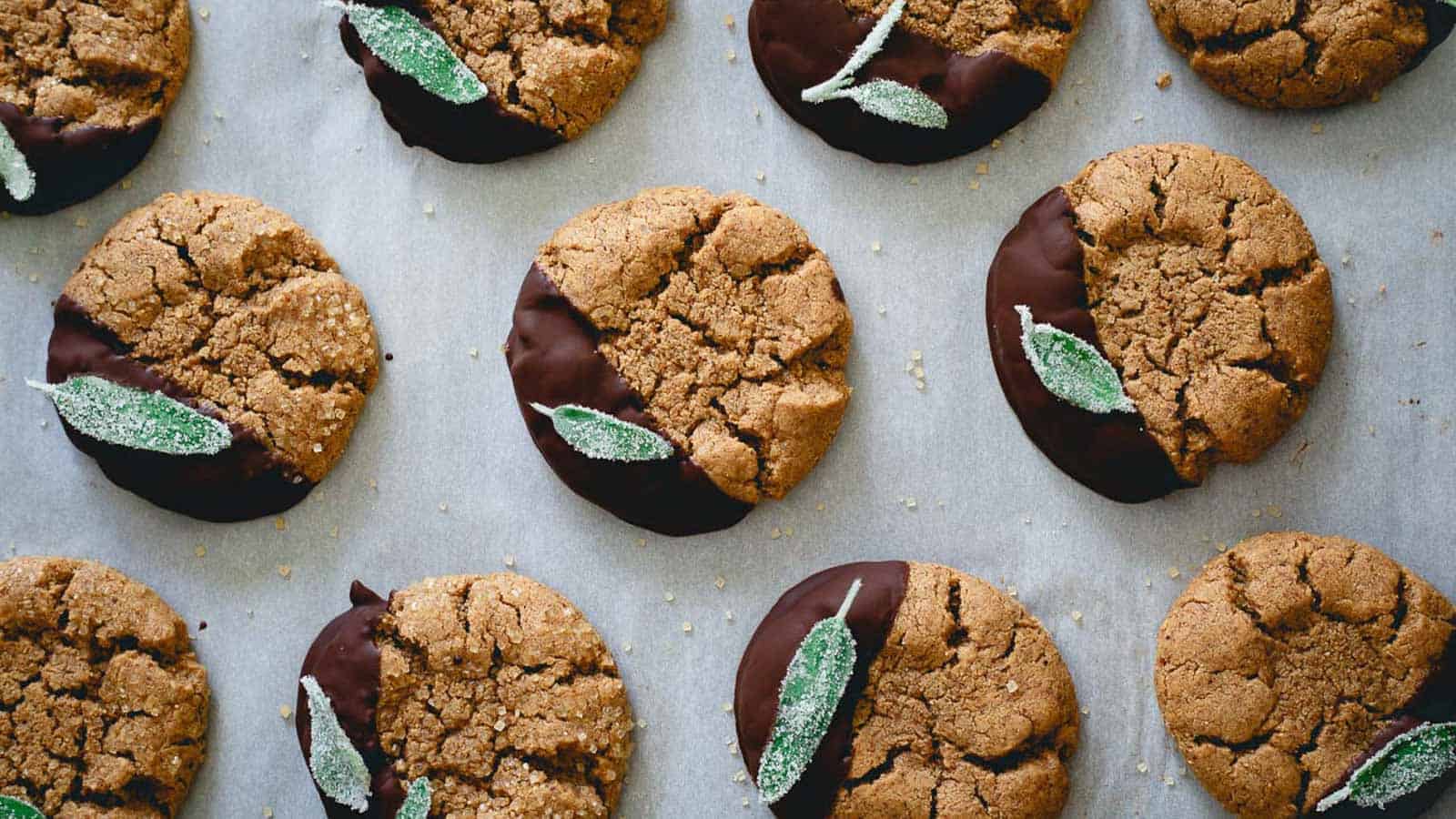 Chocolate dipped cashew almond butter cookies on parchment lined baking sheet garnished with candied sage leaf.