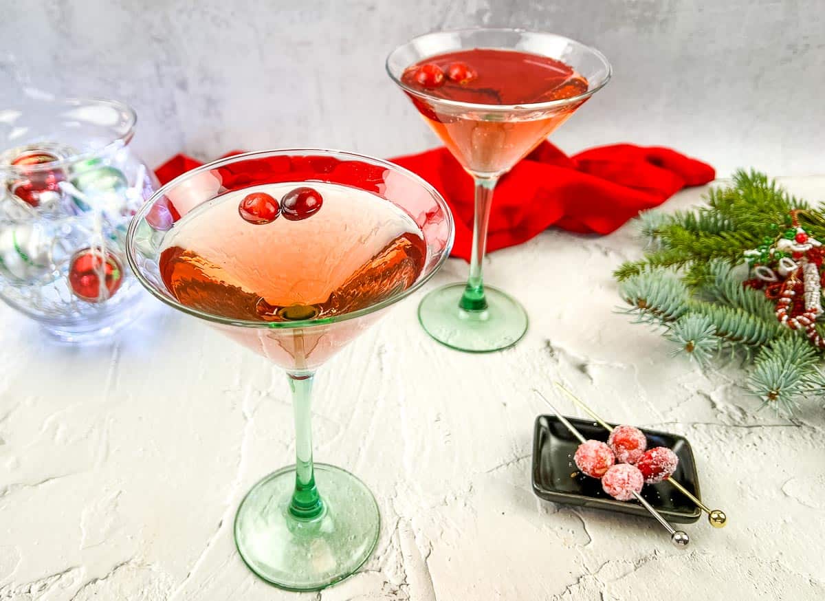 Two glasses of cranberry cosmosa and a christmas tree on a table.