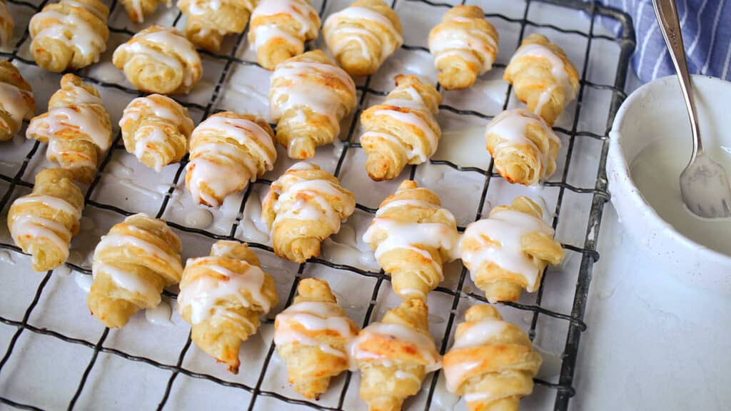 Cottage cheese rolls on a wire rack with a bowl of icing.