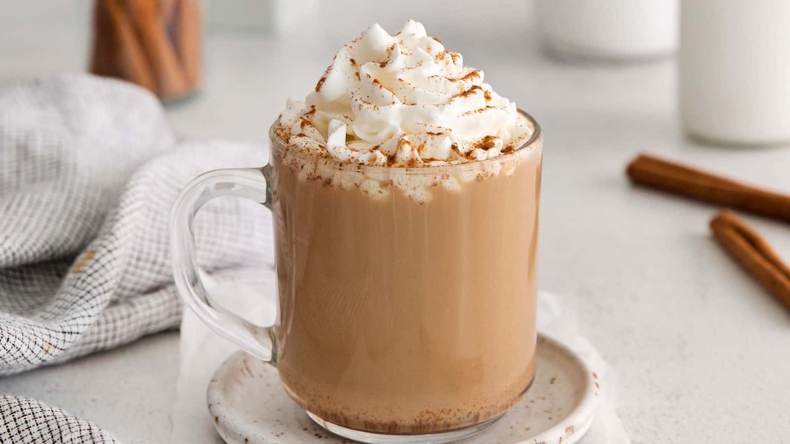 Clear mug with dolce latte and whipped cream on top with cinnamon sticks in the background.