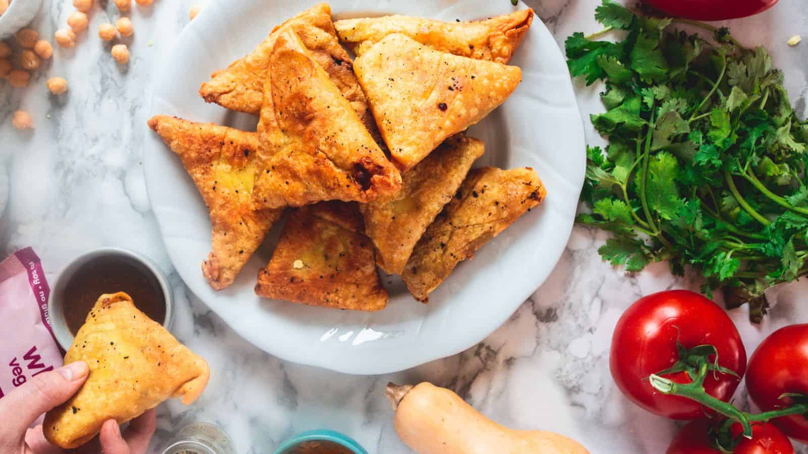 A plate with a plate of vegetables and a plate of samosas.