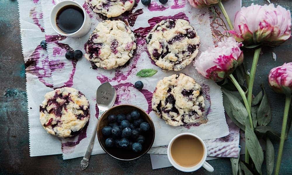 Blueberry scones with coffee and peonies on a table.