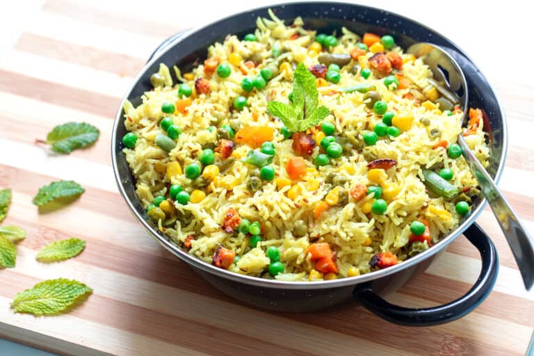 A bowl of rice with vegetables and peas on a cutting board.