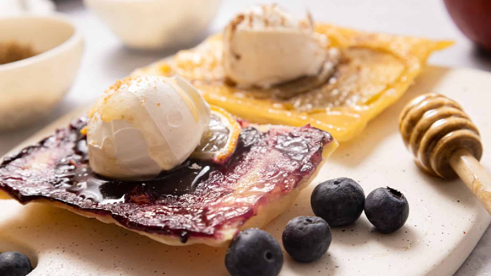 Puff pastry fruit tarts with apples and blueberries on a white board.