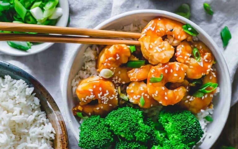 A bowl of shrimp and broccoli with chopsticks.