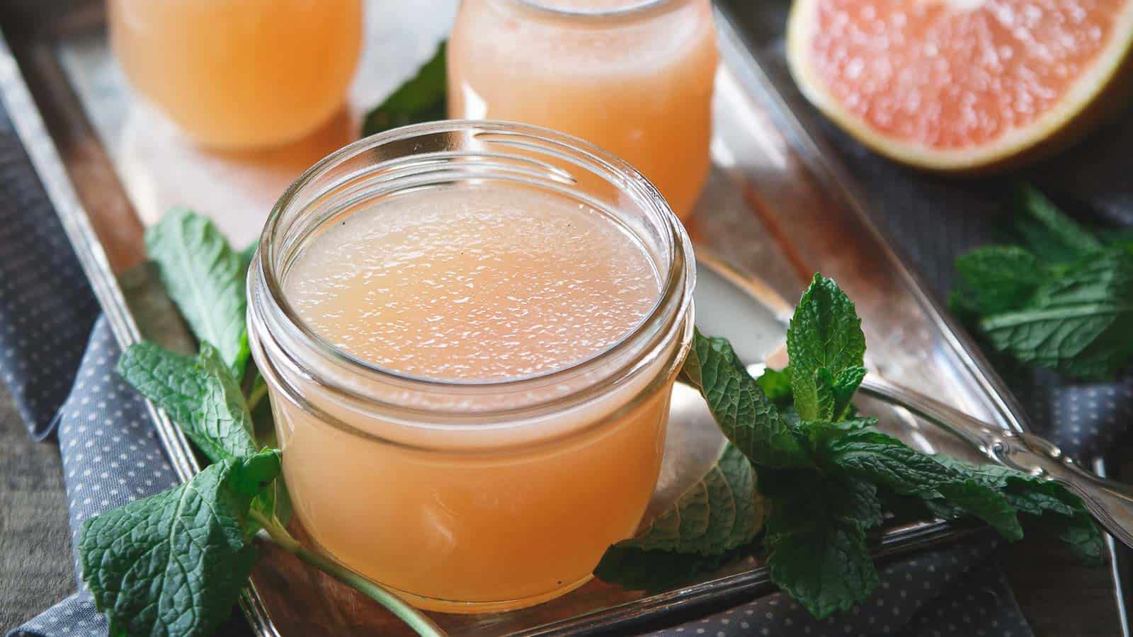 Two jars of grapefruit gelatin with mint leaves on a tray.