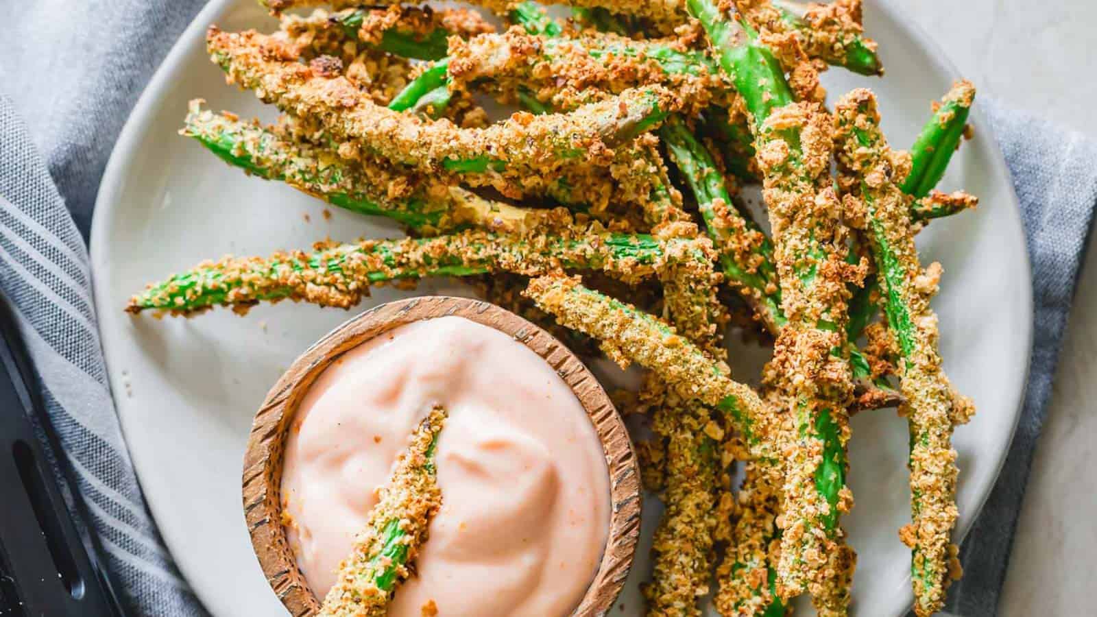 Crispy air fryer green bean fries with yogurt dip on a plate.