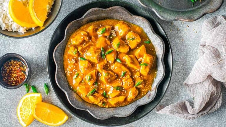 A bowl of chicken curry with orange slices and rice.