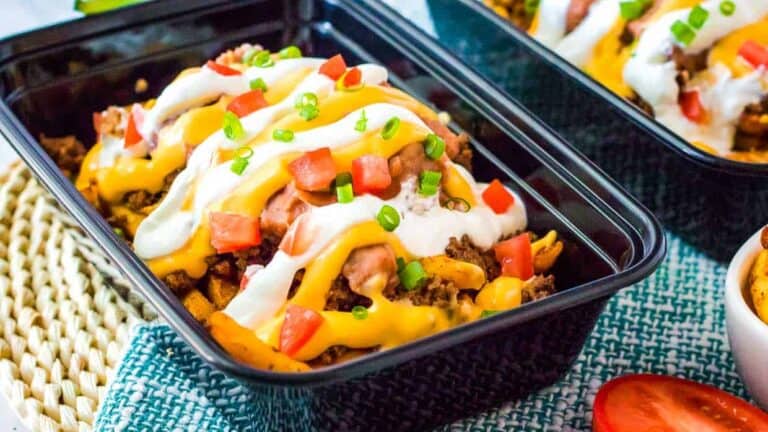 Mexican nachos in a plastic container with sour cream on top.