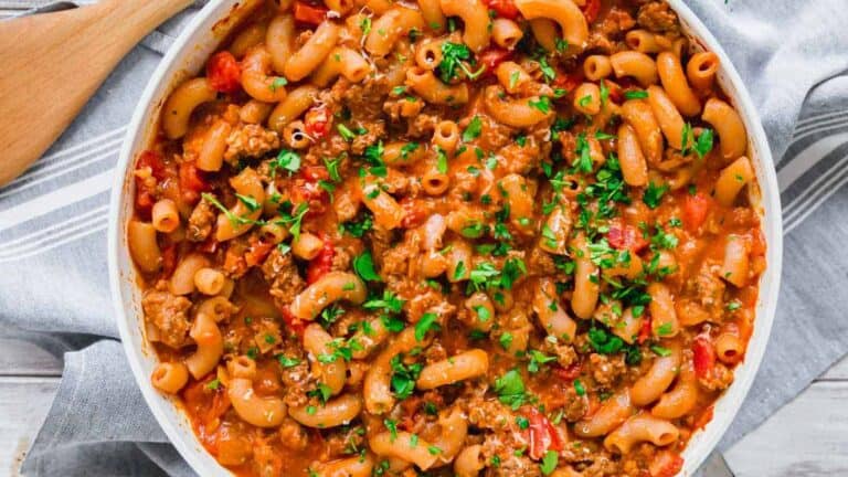 Pasta with meat and tomatoes in a white dish with a wooden spoon.