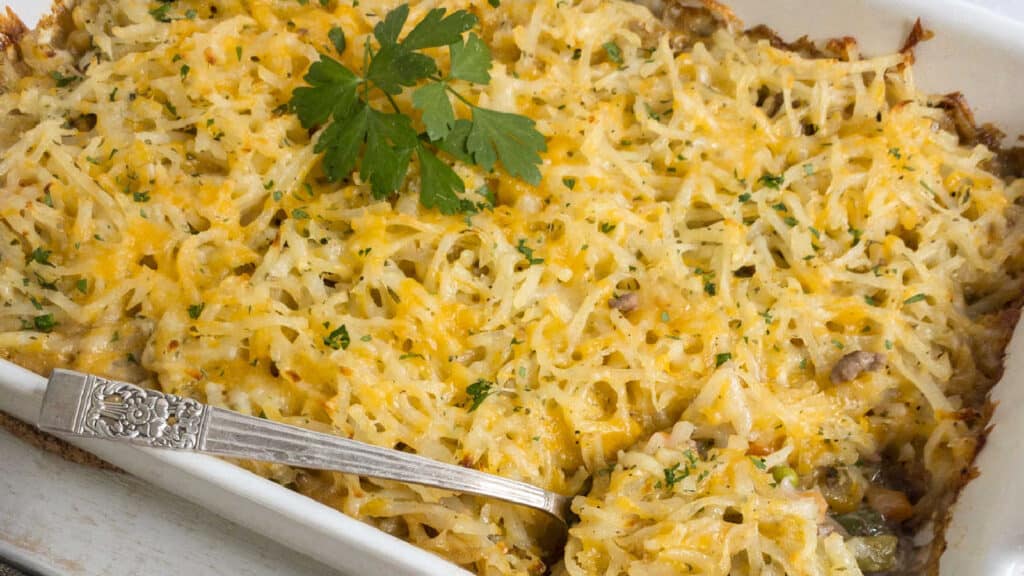 Cheesy potato casserole in a white dish with a spoon.