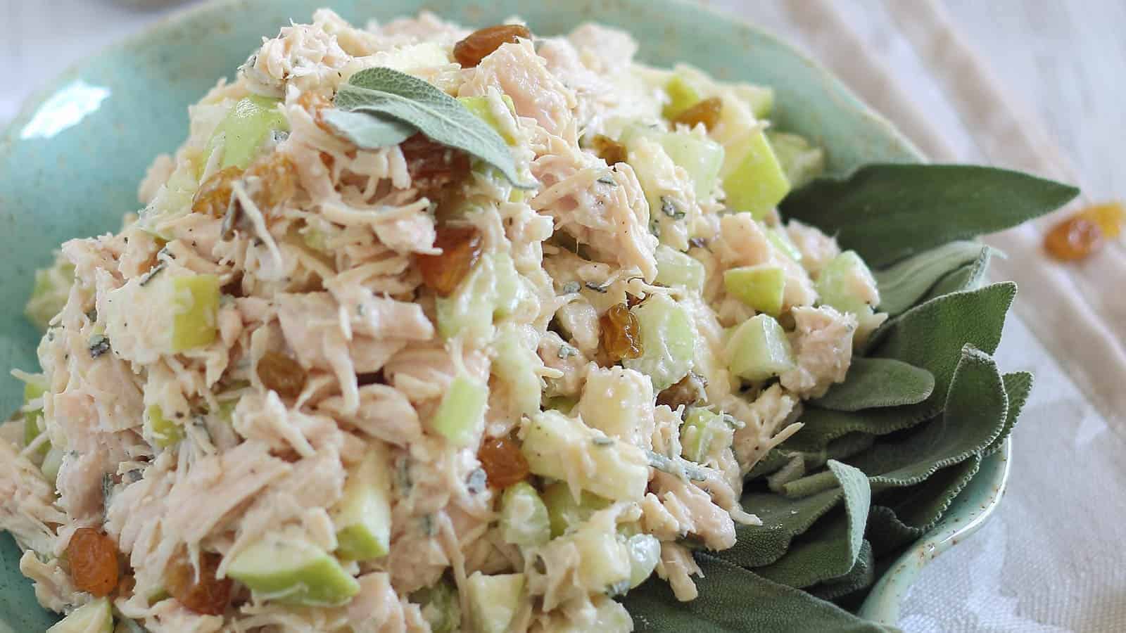 Honey apple chicken salad with fresh sage leaves in a teal bowl.