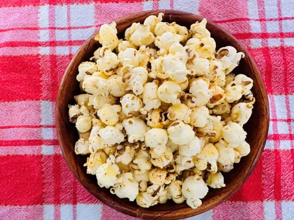 A bowl of popcorn on a red and white checkered tablecloth.
