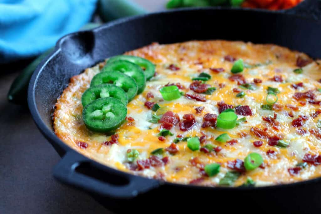 A skillet filled with jalapeno dip, bacon and jalapenos.