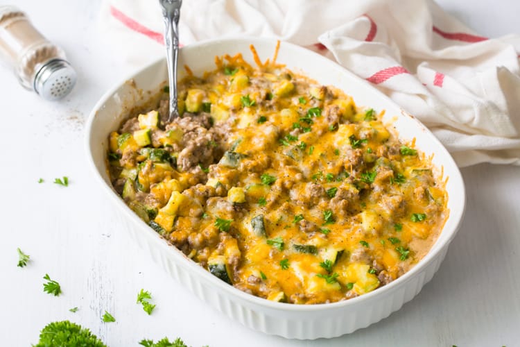 A cheese, beef and zucchini casserole in a white casserole dish topped with parsely.