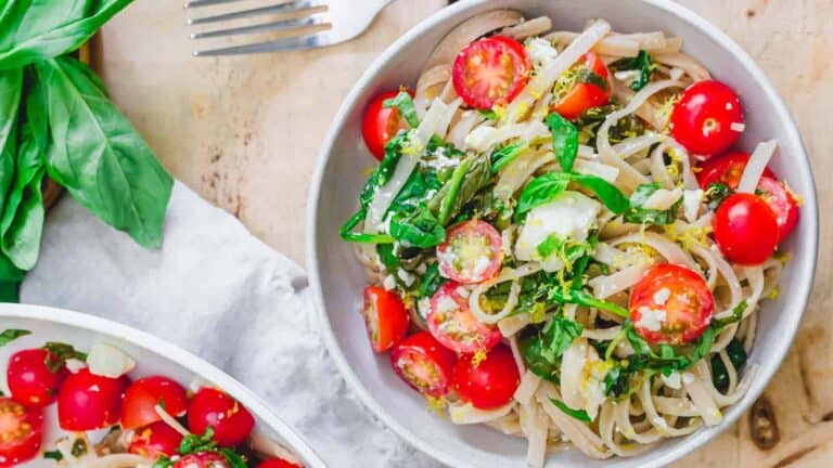 Two bowls of pasta with tomatoes and basil.