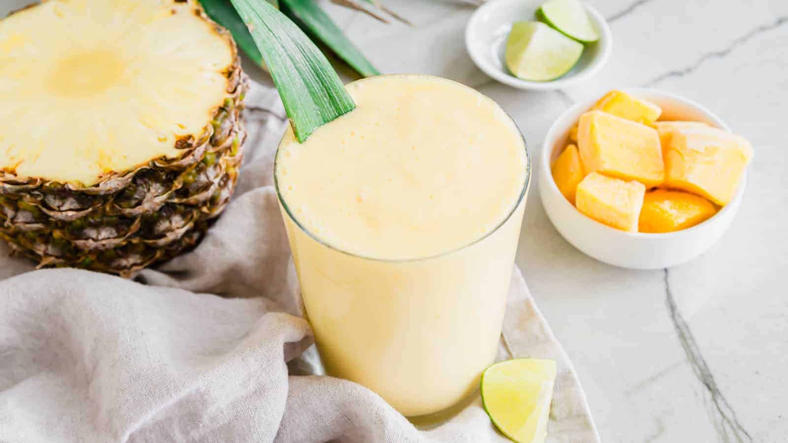 A mango pineapple smoothie on a table next to a slice of pineapple.