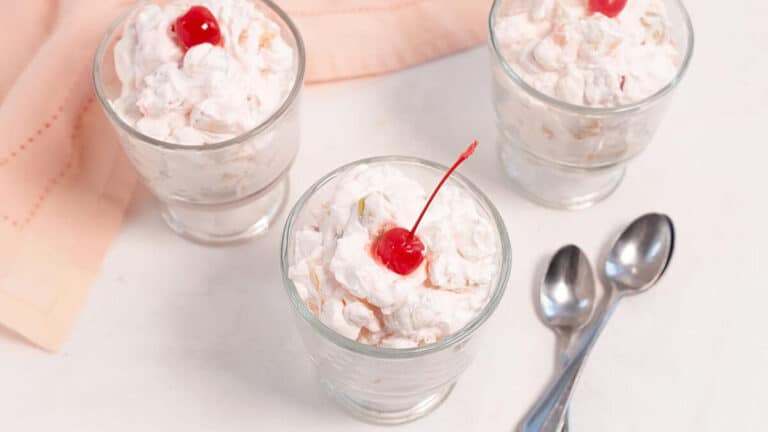 Three fruit salad desserts with whipped cream and a cherry on top.