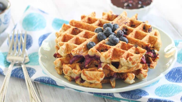 A plate with blueberry waffles and a cup of coffee.