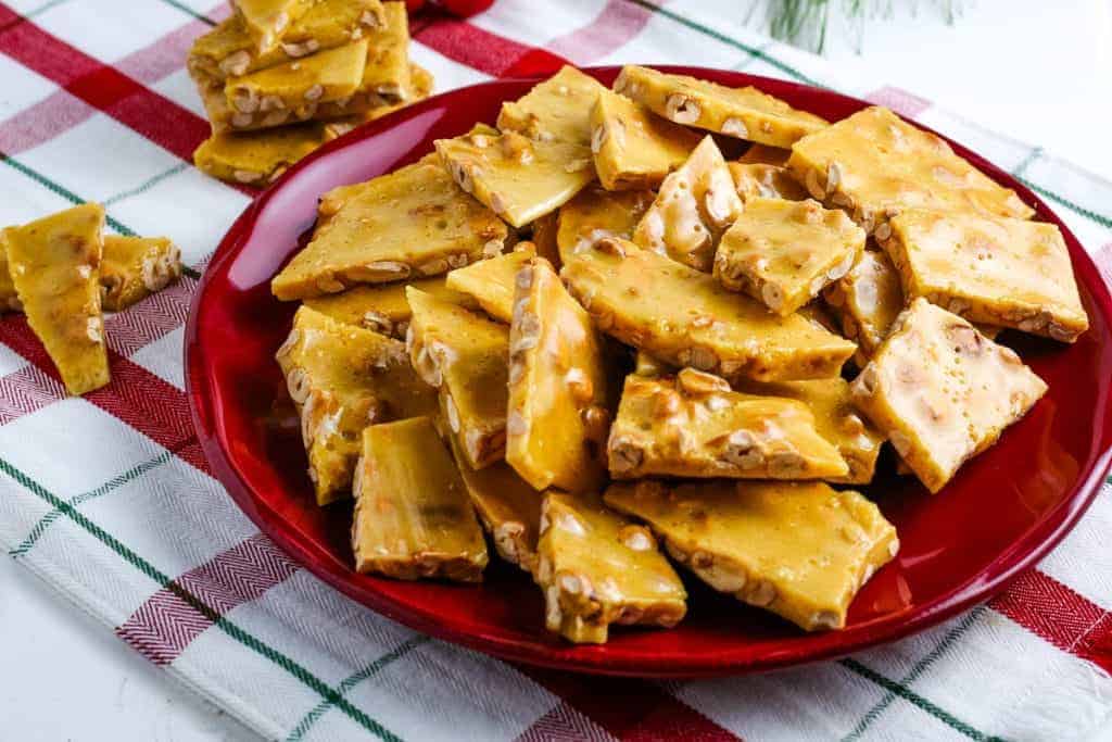 Red plate with peanut brittle on a red and white checked table cloth.