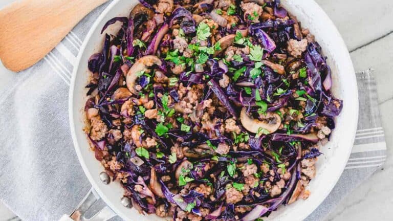 Cabbage and pork in a skillet with a wooden spoon.