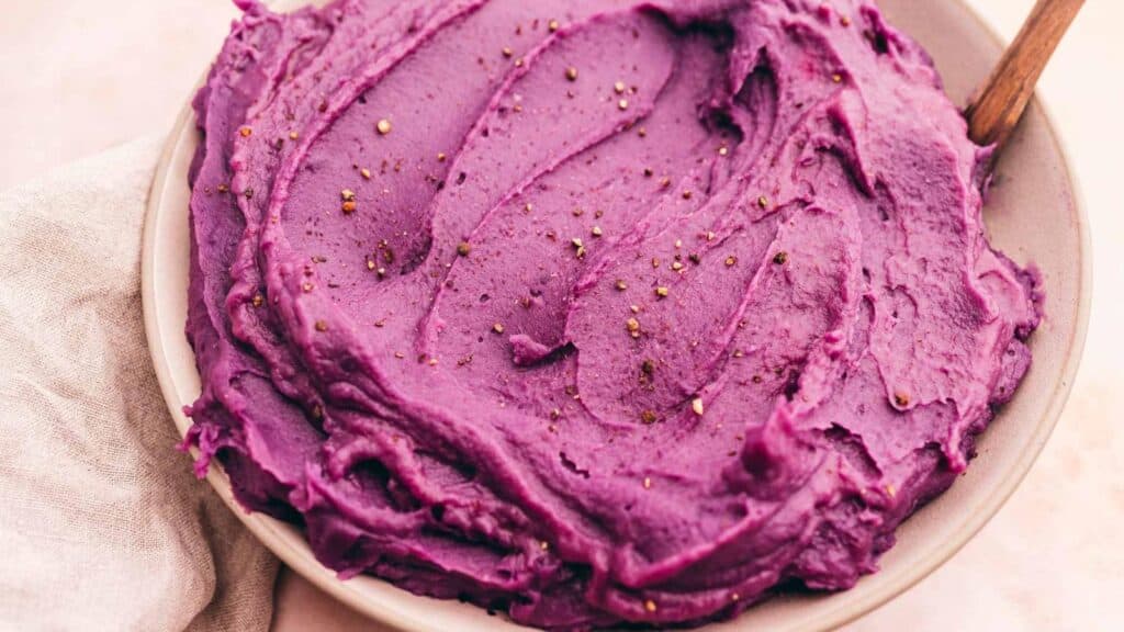 Purple mashed potatoes in a bowl with a wooden spoon.