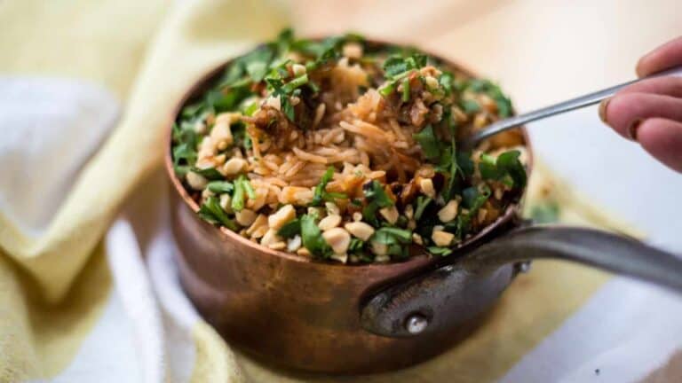 A person is holding a spoonful of rice in a copper pot.