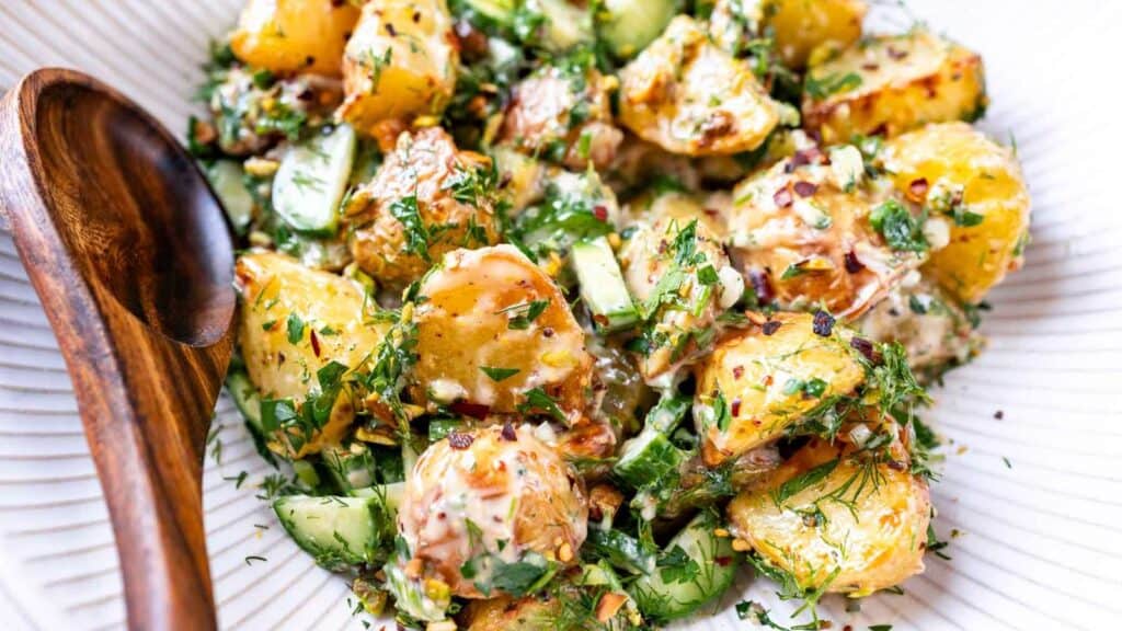 A bowl of potato salad with cucumbers and herbs.