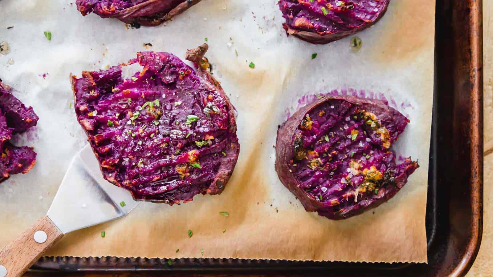 Smashed roasted purple sweet potatoes on parchment paper lined baking sheet.