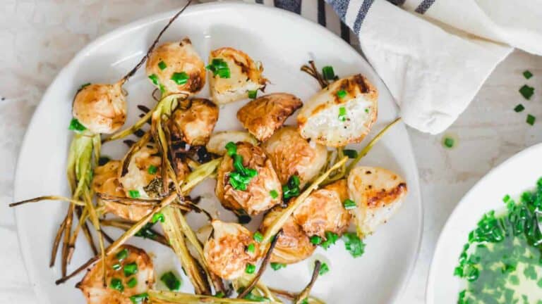 Roasted turnips on a white plate with greens.