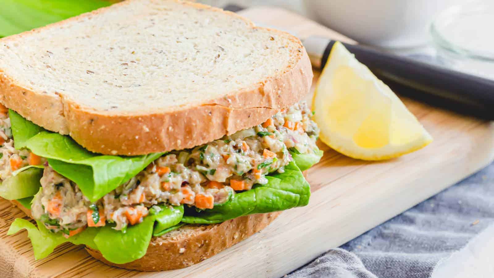 Sardine salad sandwich on a cutting board with a lemon wedge.