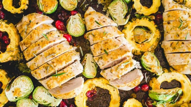 Roasted chicken with cranberries and brussels sprouts on a baking sheet.