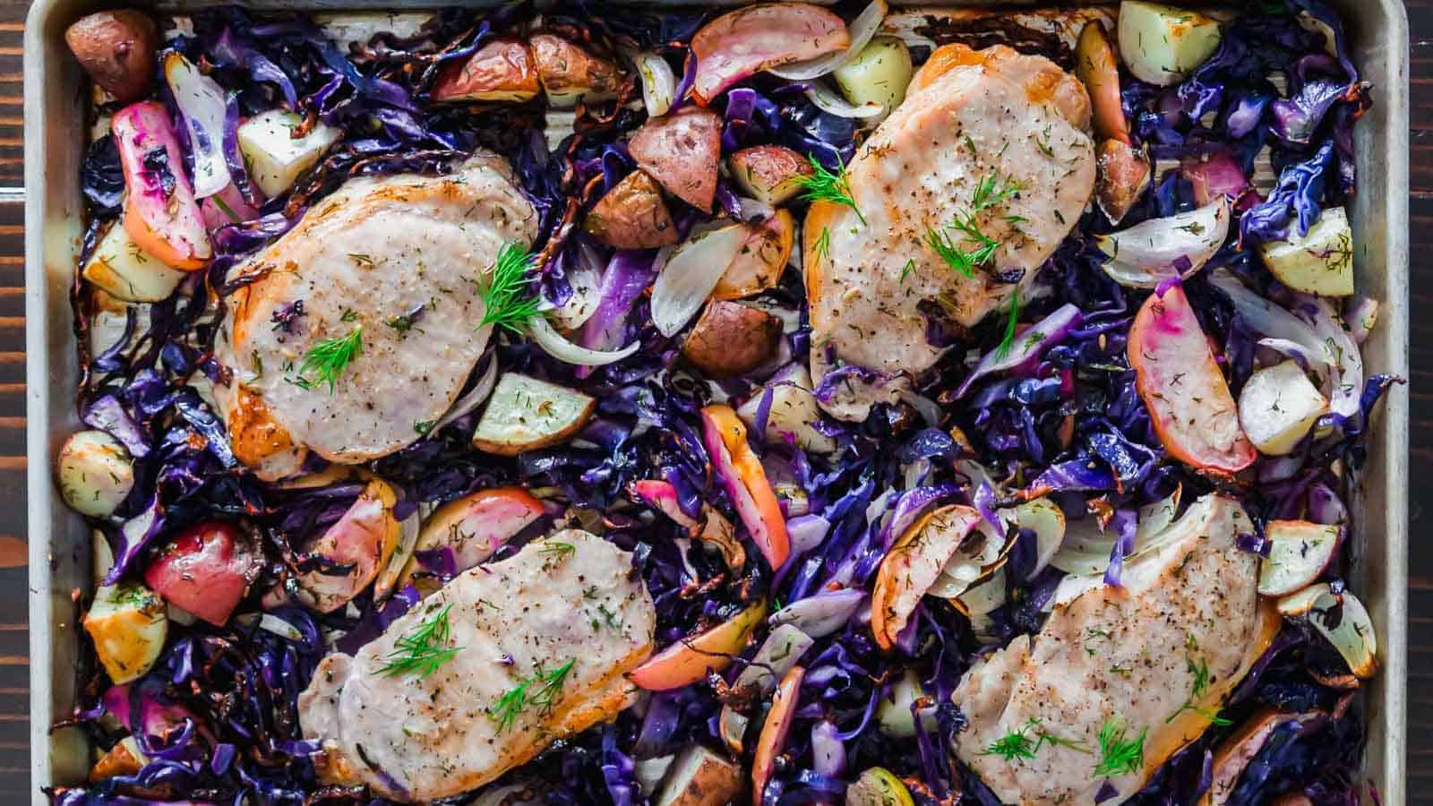 Pork chops with purple cabbage and apples on a baking sheet.