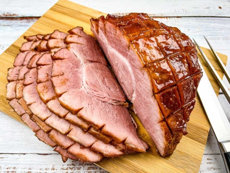 Ham on a cutting board with a knife and fork.