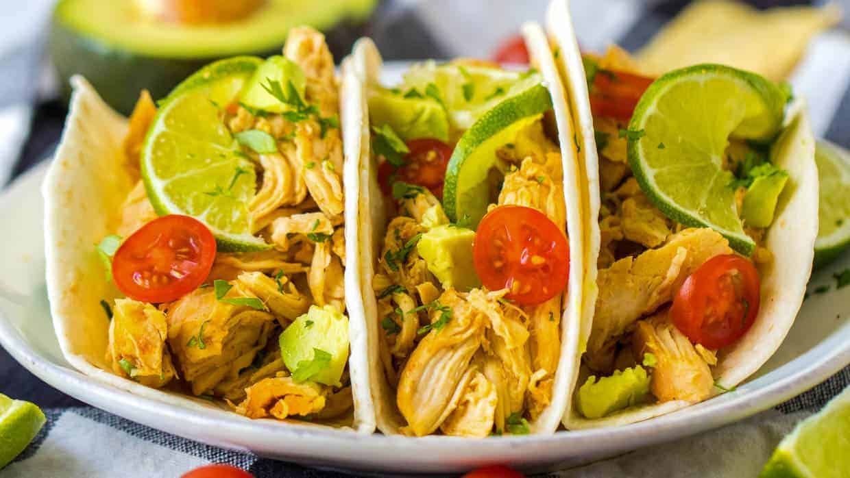 Three slow cooker tacos with chicken, lime, avocado and tomatoes.