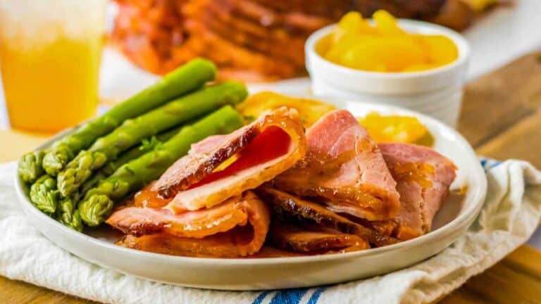 A plate of ham and asparagus with a glass of orange juice.