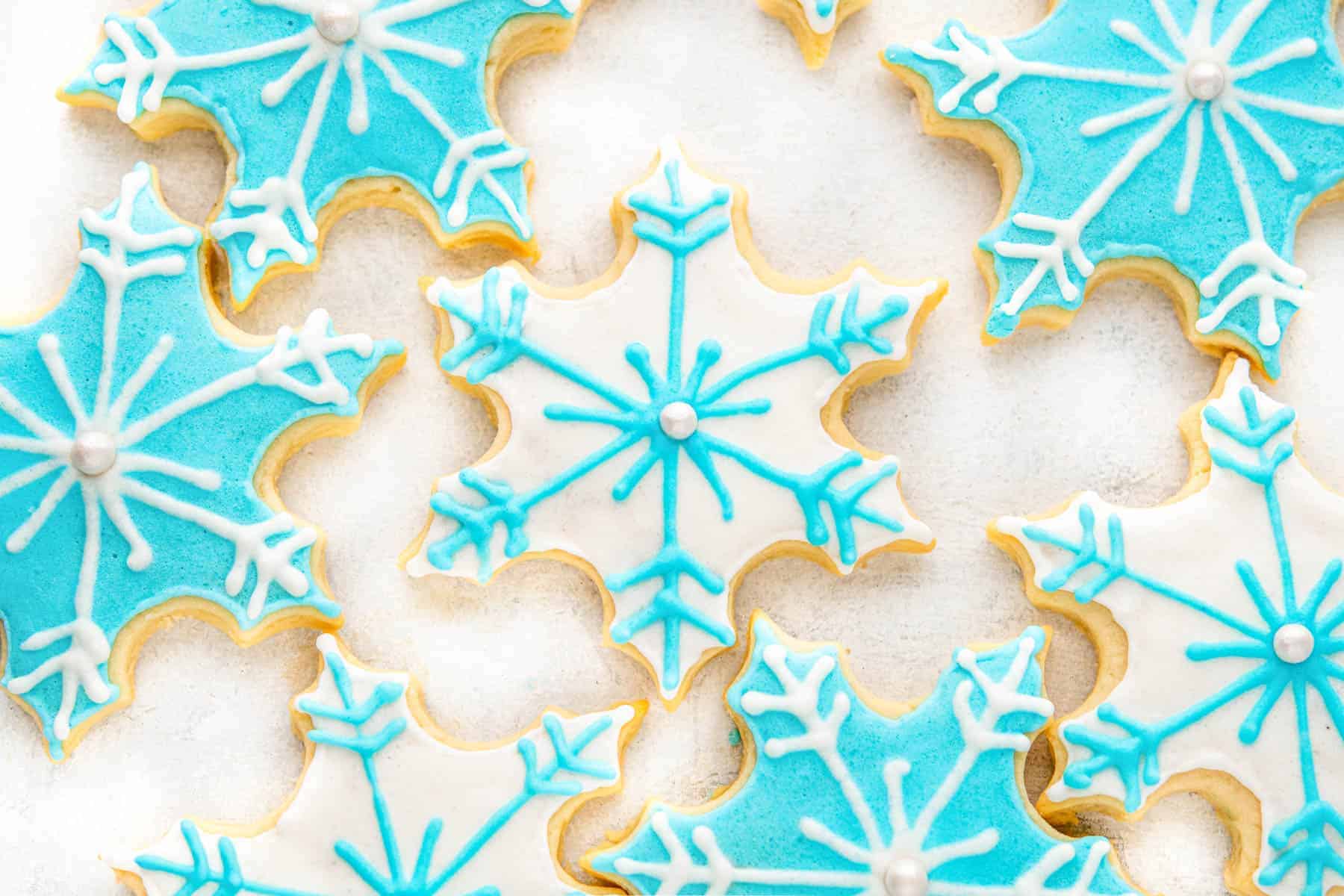 Festive blue and white sugar cookies shaped like snowflakes on a white background.
