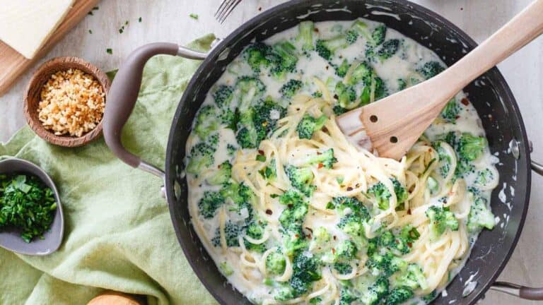 A pan full of pasta and broccoli with a wooden spoon.