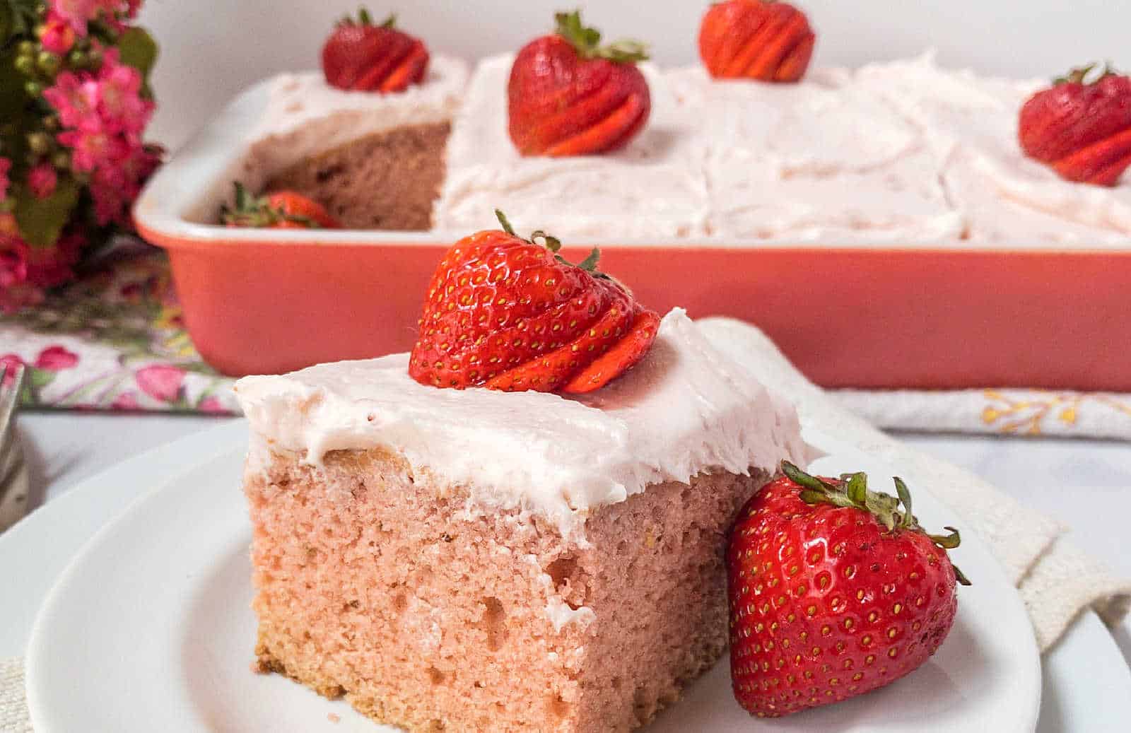 A slice of homemade strawberry cake with icing and strawberry on top.