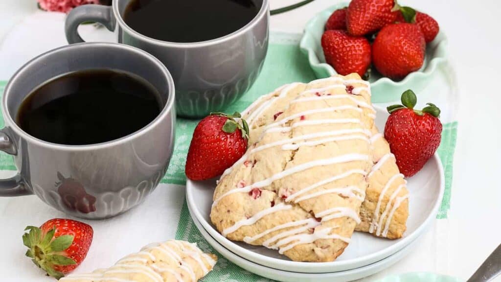 Strawberry scones on a plate next to a cup of coffee.