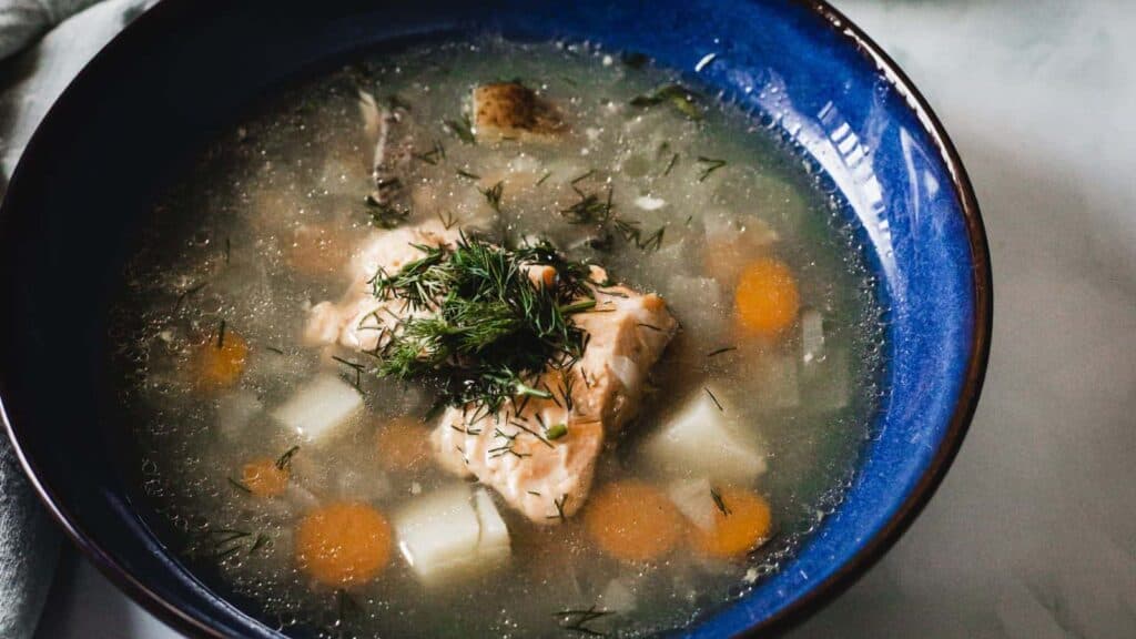 A bowl of soup with fish and vegetables in it.