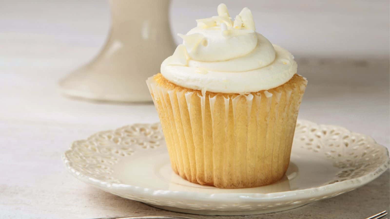 Vanilla cupcake with frosting on white china plate.