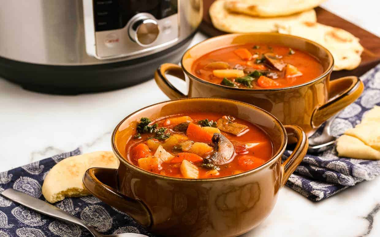 Two bowls of instant pot vegetable soup in front of the pressure cooker.