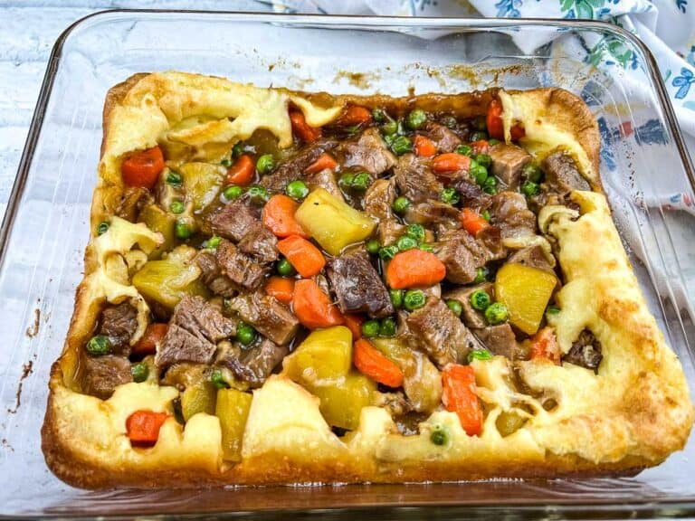 A casserole dish filled with beef, carrots and peas.