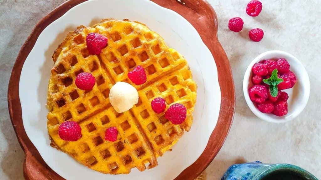 A plate with waffles and raspberries on it.