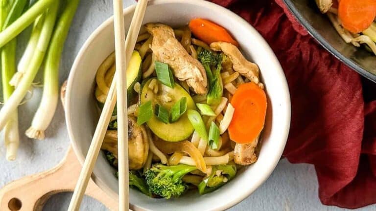 A bowl of chicken stir fry with vegetables and chopsticks.