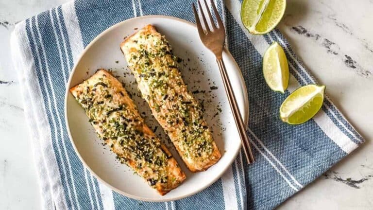 Furikake topped salmon on a white plate surrounded by sliced limes.