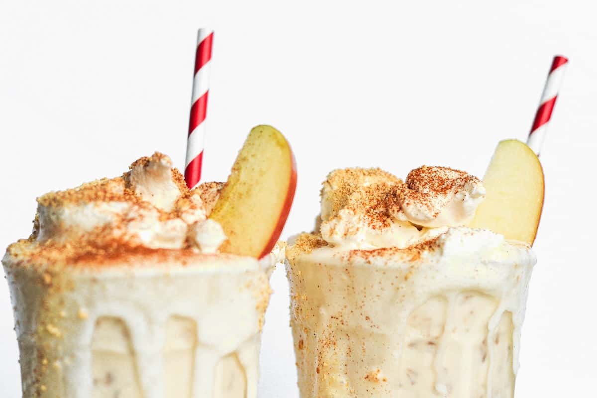 Apple pie milkshake with a straw and apple slices.