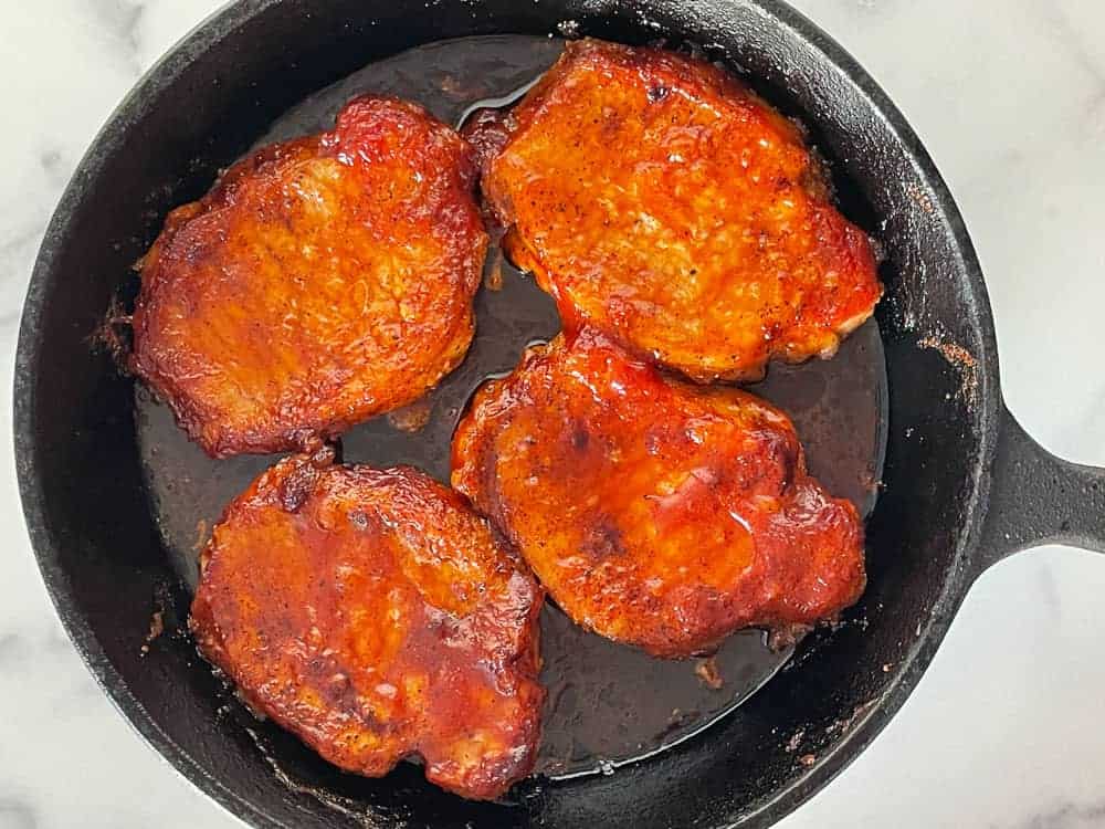 Pork chops in a cast iron skillet with bbq sauce on the chops.